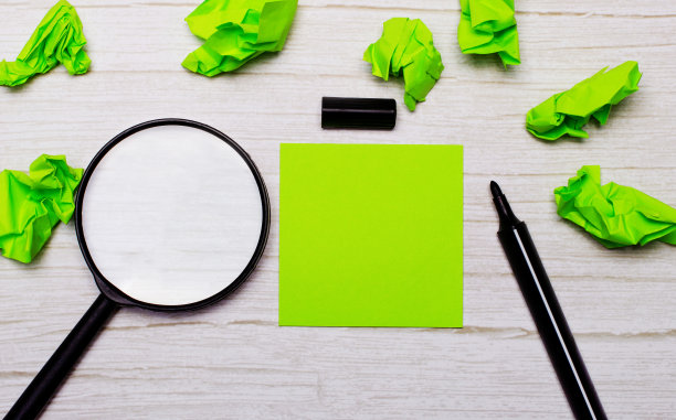 木桌上放着一个放大镜，一张绿色的贴纸，上面有一个可以用来复制文字或图片的地方，还有一个记号笔。经营理念图片下载