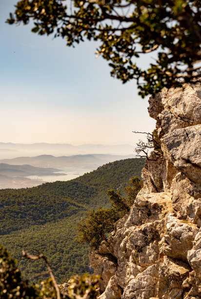 这幅田园诗般的照片展示了一个有岩石和树木的山峰。大海和蓝天，背景是云。图片下载