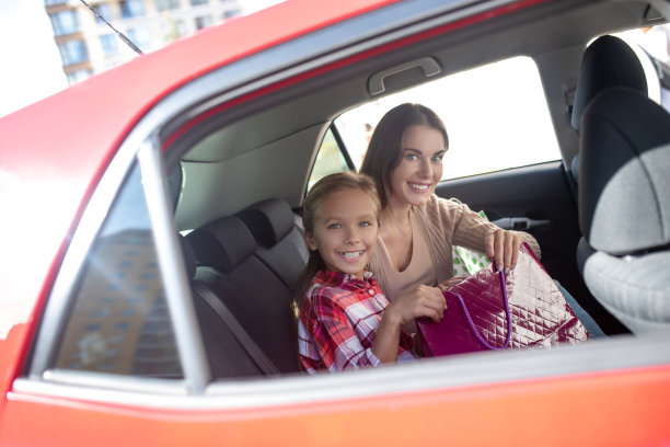微笑的女孩和她的妈妈坐在后座上购物袋图片下载