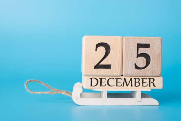 等待的日子概念。木制日历的特写照片显示12月25日站在雪橇上孤立的蓝色背景图片下载