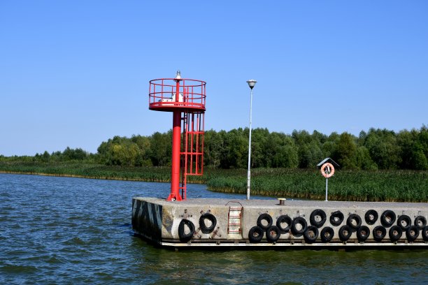 在一个混凝土码头或码头的边缘有一个梯子，可以看到一个红色的观察塔，在一个阳光明媚的夏天，船更容易停靠在那里图片下载