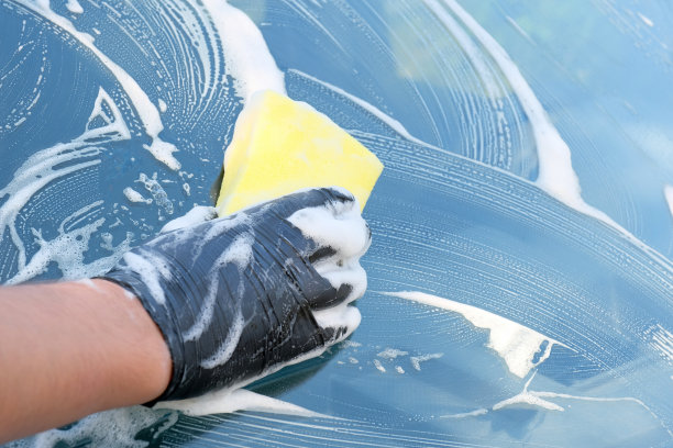 用肥皂洗车。一个戴黑手套的男人用海绵擦拭挡风玻璃。车停在泡沫。图片下载