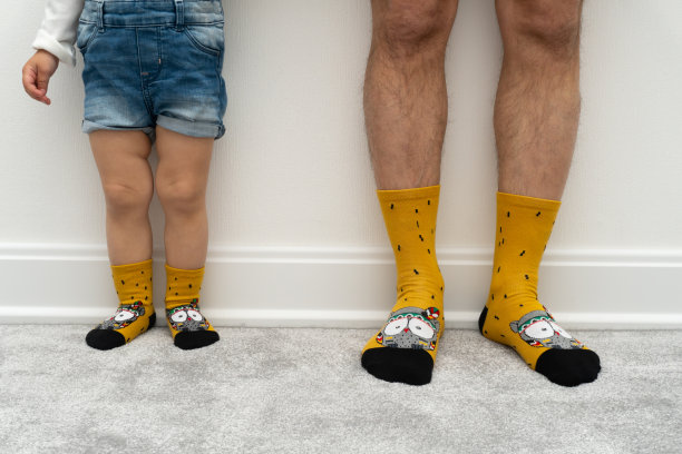 穿着相同服装的家庭，白人父亲和孩子穿着相同的黄色袜子，只有腿在白色墙壁附近的灰色地毯上，有复制空间。图片下载