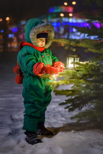 冬天的晚上，小男孩站在明亮的圣诞树旁图片下载