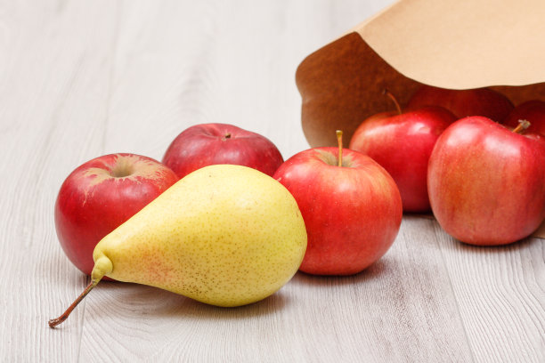 木桌上放着熟梨和红苹果和纸袋。图片下载
