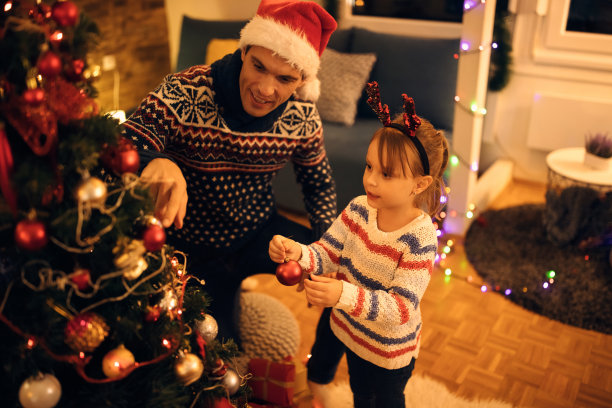 可爱的小女孩在家里和爸爸一起装饰圣诞树。图片下载
