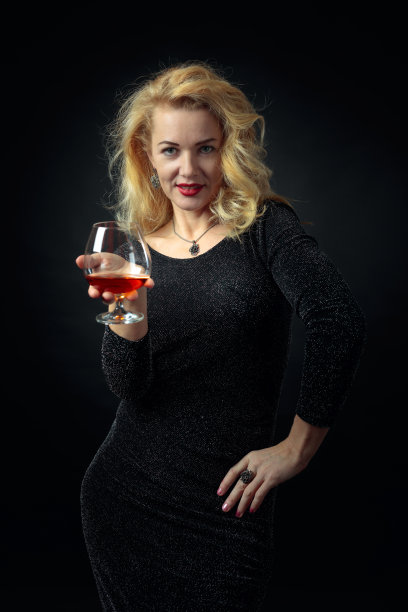 迷人的成熟女人穿着黑色晚礼服和白兰地的气味。图片下载