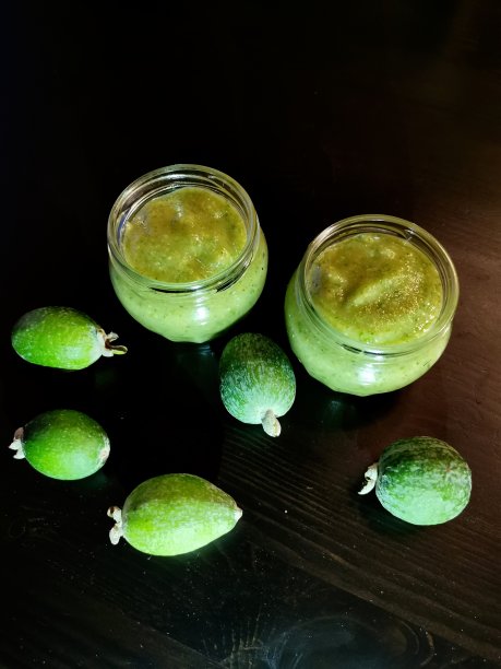 两个玻璃罐与捣碎的feijoa糖和新鲜的feijoa在黑色的桌子背景图片下载