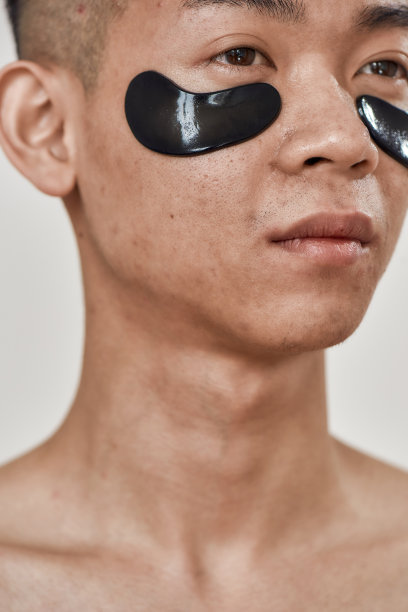 近距离的面部皮肤的年轻亚洲男子与黑眼圈下，看远离孤立的白色背景。美容，日常护肤，男士美容图片下载