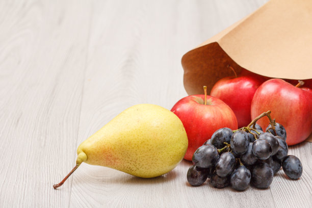 熟透的梨子、葡萄、红苹果和纸袋放在木桌上。图片下载