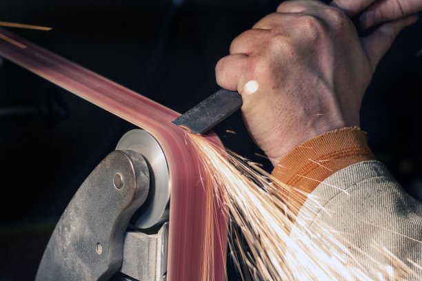 在砂带磨床上磨制刀片的过程。刀制作大师的双手合上。图片下载