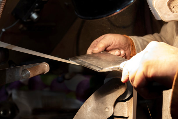 在砂带磨床上磨制刀片的过程。刀制作大师的双手合上。图片下载