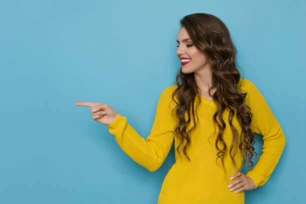 穿着黄色毛衣微笑的年轻女子看向别处并指着图片下载