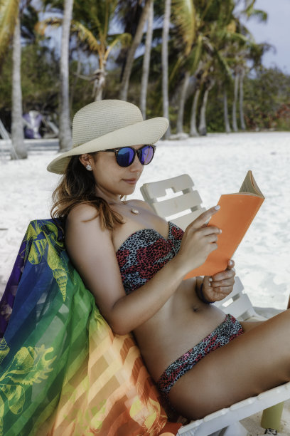 一名西班牙裔年轻女子在加勒比海的一个热带白沙岛上的沙滩上看书图片下载