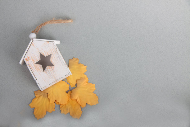 木制的玩具屋和黄色的树叶在灰色的背景上平躺着图片下载