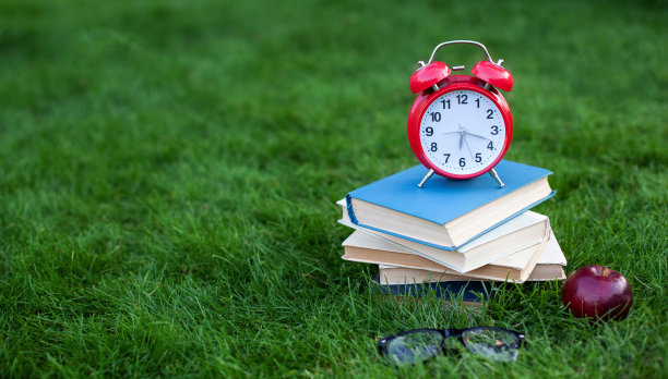 秋季早晨，公园里的红色闹钟和旧书堆放，理念教育和阅读。书、苹果、带闹钟的眼镜躺在学校附近的草地上。副本的空间。模型。回到学校。图片下载