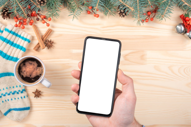 圣诞节模型手机。模型智能手机上模糊的圣诞节背景与圣诞装饰白色木制桌子。图片下载