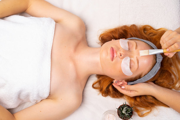 水疗中心。美容师用刷子给小女孩敷上透明面膜。健康、滋润、护肤的理念图片下载