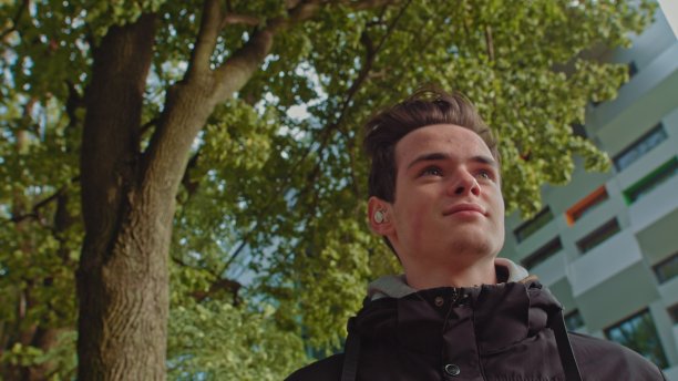 一个年轻人在外面用无线耳机打电话，一边走在街上。年轻人，青少年戴着现代无线耳机。一个年轻人的肖像图片下载