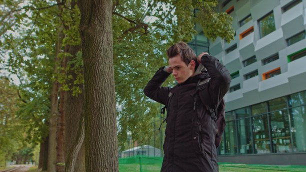 一个时髦的年轻人戴着兜帽看着镜头的肖像。近距离观看千禧男孩在黑色帽衫微笑站在街上。人的情感概念图片下载