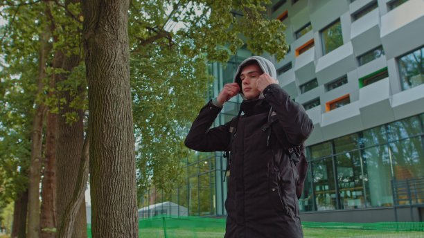 一个时髦的年轻人戴着兜帽看着镜头的肖像。近距离观看千禧男孩在黑色帽衫微笑站在街上。人的情感概念图片下载