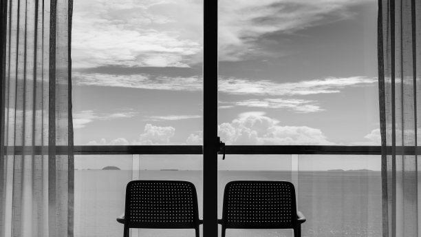 从阳台上的2张椅子的窗口后视图，黑白色调的海景和天空。图片下载
