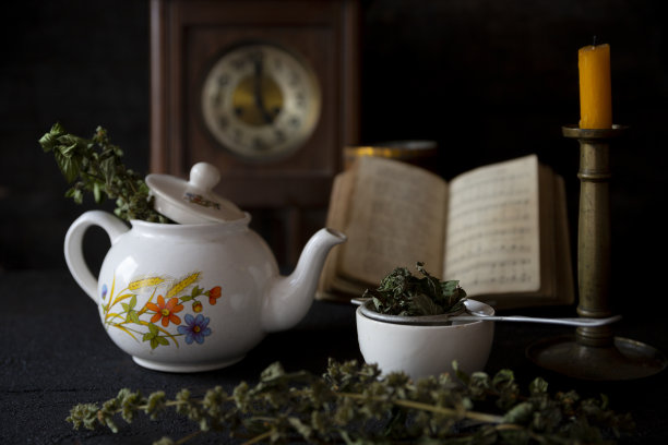 一杯茶和茶壶在木桌上，旧时钟，蜡烛和书的背景图片下载