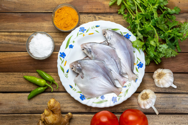 新鲜的白鲳鱼与生姜，大蒜，青辣椒，香菜叶和香料一起放在木板上。图片下载