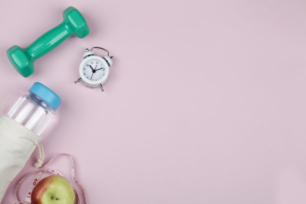 健身、健康、积极的生活方式理念。哑铃，一瓶水，苹果，闹钟和粉红色背景的卷尺。为文本复制空间。俯视图图片下载
