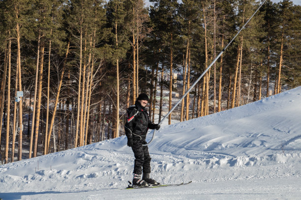 一名穿着滑雪服、面带微笑的男子在积雪覆盖的斜坡上用拖曳式电梯滑雪。图片下载