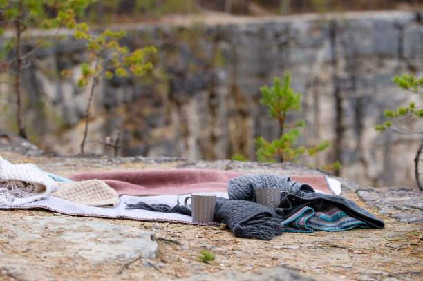 一条毯子，一件针织品和两个杯子躺在山的边缘。图片下载