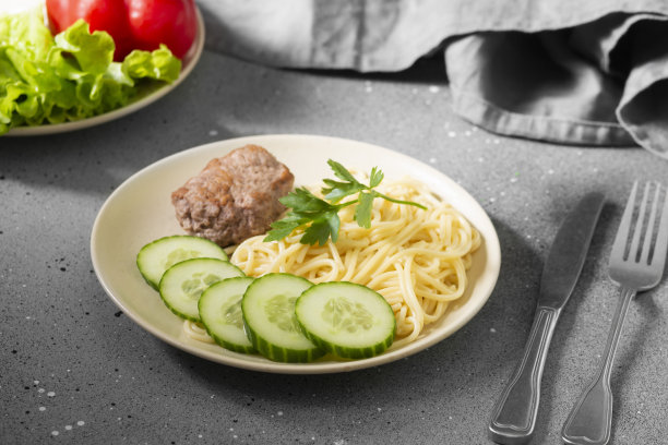 灰色的桌子上米色的盘子里放着意大利面、肉片和黄瓜图片下载