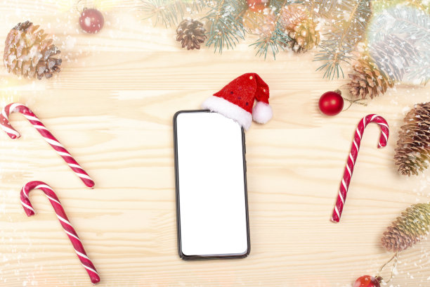 模拟智能手机与空白的白色屏幕与圣诞老人帽的办公桌圣诞背景，平躺与空白屏幕为您的圣诞快乐和新年快乐的文本图片下载