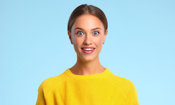幸福的情绪惊讶的女人在黄色毛衣上的蓝色背景图片下载