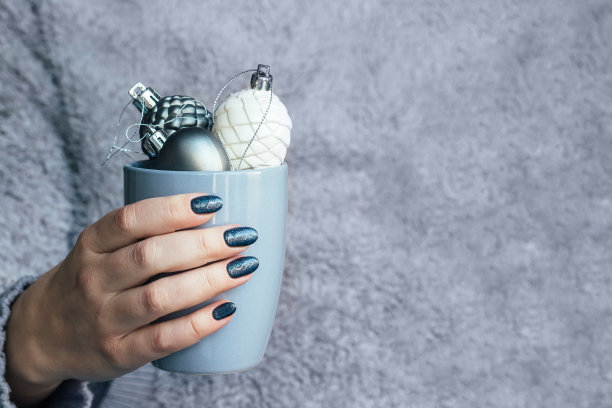 女性手在灰色毛茸茸的针织毛衣与美丽的美甲-深灰色蓝色闪闪发光的指甲杯与圣诞装饰与拷贝空间图片下载