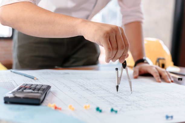 建筑师使用分度罗盘工作蓝图。桌上有蓝图，尺子，计算器，安全帽和书。建筑的概念。工程工具图片下载