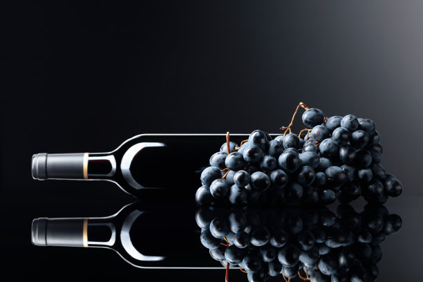 一瓶红酒和一串葡萄在黑色的反光背景。图片下载