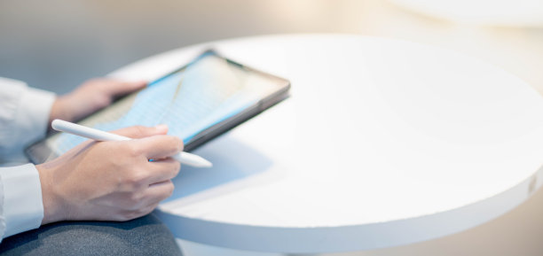 一个女人拿着这个小工具在线阅读，坐在一个有社交距离概念的共同工作空间里。图片下载