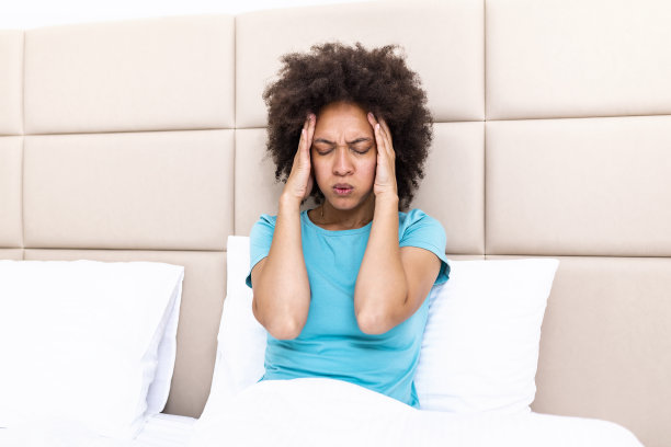 一个漂亮的黑人妇女坐在家里的床上，头疼，感觉疼痛，表情不舒服。图片下载
