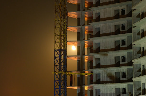 半月形的月光穿过新多层建筑的混凝土结构。秋夜在工地上。抽象的闪烁灯光效果。基辅,乌克兰图片下载