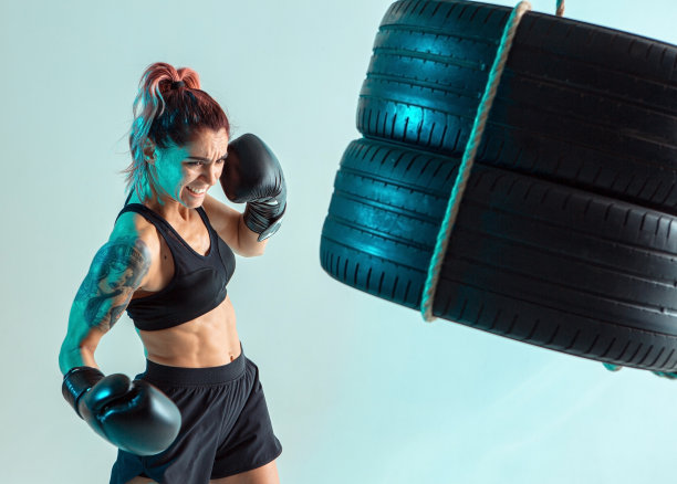 一个女拳击手在拳击手套打击轮胎与她的手图片下载