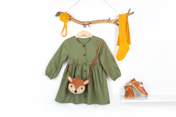 一套时尚的儿童服装。衣架上有绿色的裙子，棕色的包和黄色的紧身衣，木棒上的头发饰品，架子上的鞋子。时尚女孩lookbook概念，正面视图图片下载