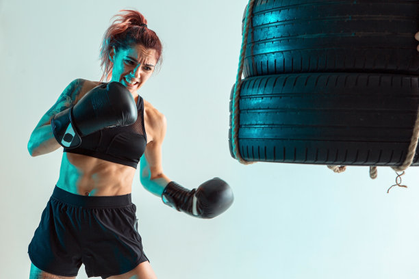 一个女拳击手在拳击手套打击轮胎与她的手图片下载