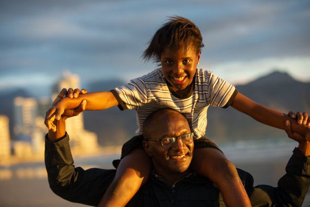日落时分的海滩上，女儿坐在爸爸的肩膀上图片下载