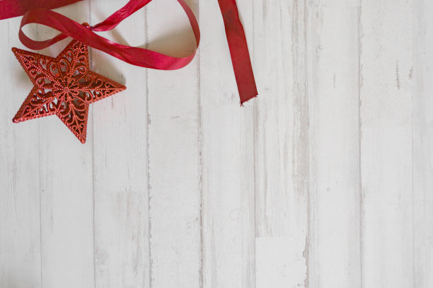 红色的圣诞星用红色的蝴蝶结装饰放在圣诞树上，以白色的木头为背景来庆祝圣诞节图片下载