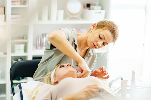 美丽快乐的白人女人微笑，而做面部按摩客户在水疗中心-女性美容师医生美容师在沙龙面膜-保健概念复制空间图片下载