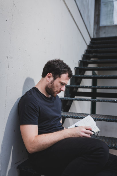 那个在金属楼梯上读书写字的年轻人。图片下载