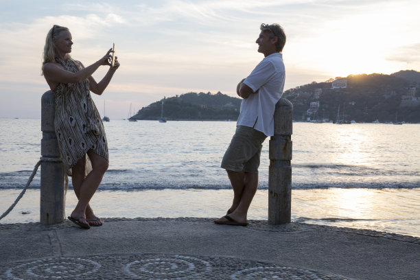 日落时分，一对情侣在海滩上用平板电脑拍照图片下载