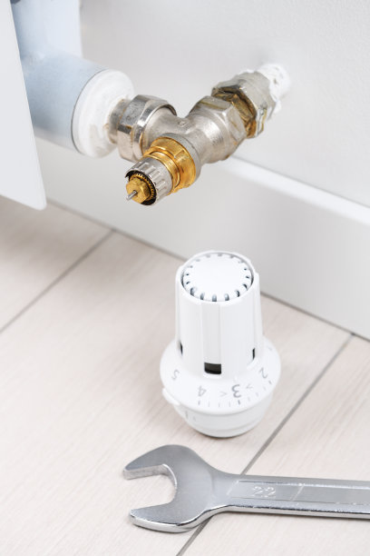 在一间公寓办公室里，一个扳手躺在加热电池恒温器旁边的地板上。加热的复苏。图片下载