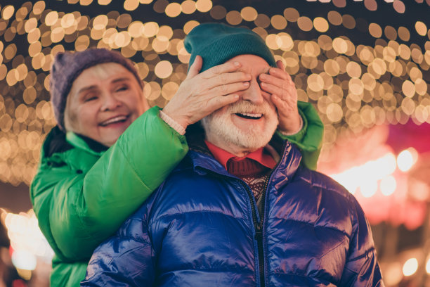 两名老人的照片，白发，已婚的夫妇，女人close cover脸，手，丈夫想走圣诞夜在灯光下的户外约会图片下载